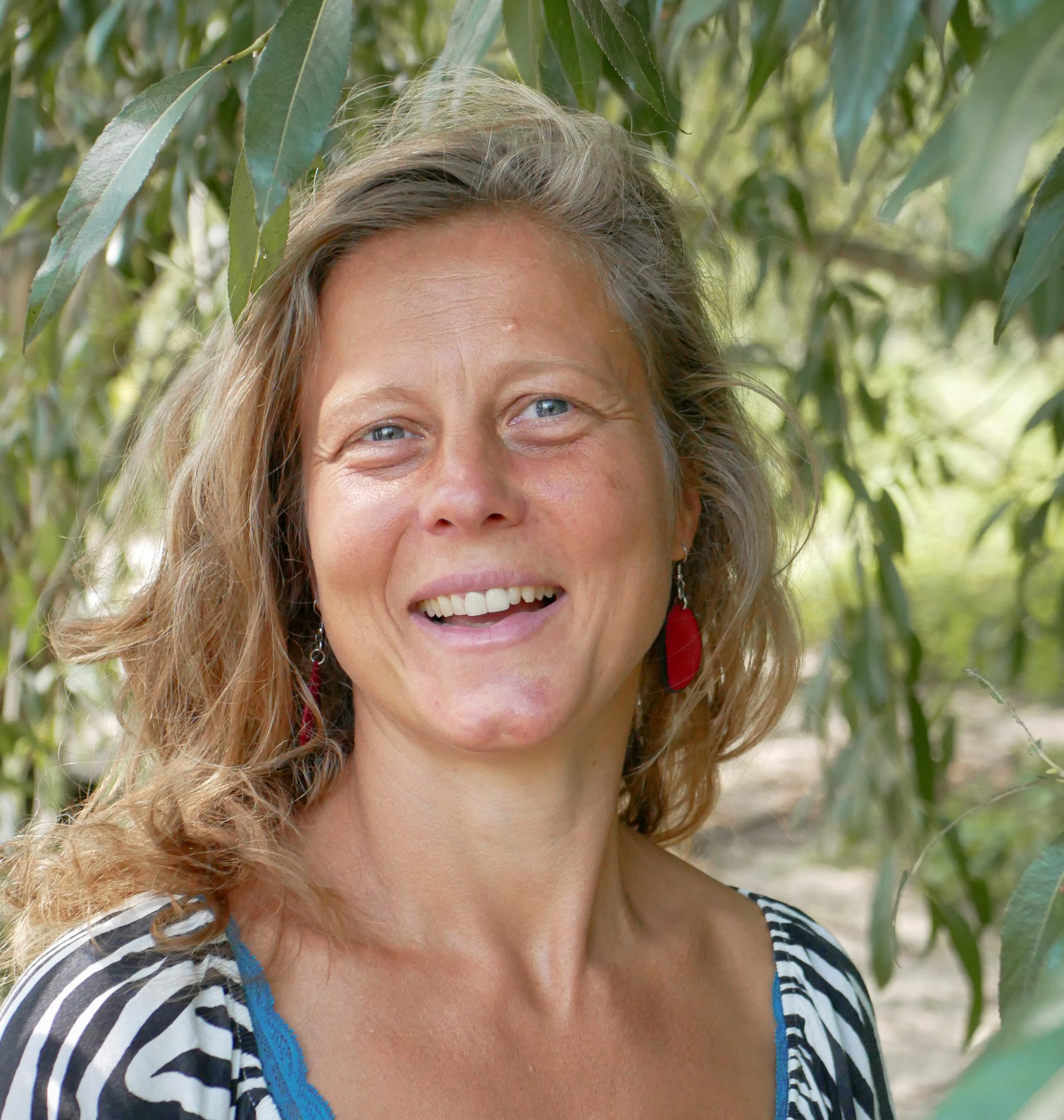 Nina Horn lächelt in die Kamera, umgeben von grünen Zweigen