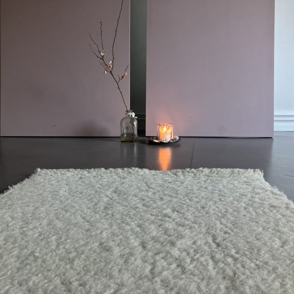 Heller Raum mit Teppich, Kerze und Vase mit Zweig